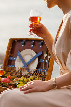 Young girl is drinking rose wine near the sea. Picnic basket with fruits in front. Relaxed atmosphere. Italy, Cinque Terre.