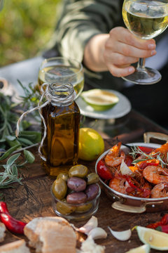 Young girl is holding a glass of white wine in her hand. Delicious italian food on the table: fried spicy shrimps in copper pan, olive oil, bread, olives. Light healthy meal, tasty snack