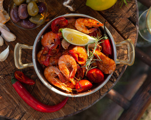 Delicious italian food. Anti-pasti: spicy fried shrimps with tomatoes, garlic and fresh herbs. Served on rustic dark wooden board in copper pan with slice of lemon. Healthy and tasty lunch. Top view