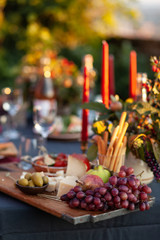 Fototapeta na wymiar Dinner party outside to celebrate special occasion. Light snacks, fruit, cheese. Red candles as decor. Relax atmosphere, festive mood