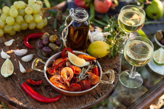 couple: copper pan with delicious and spicy fried shrimps with herbs and garlic, wine, bread, olives. Bottle of olive oil. Luxury lifestyle, gourmet food