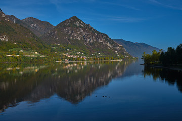Naklejka na ściany i meble Panoramic view of the mountains and Lake Idro. Autumn season, the reflection in the water of the mountains, trees, blue sky