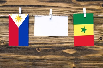 Hanging flags of Philippines and Senegal attached to rope with clothes pins with copy space on white note paper on wooden background.Diplomatic relations between countries.