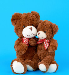 two brown teddy bears with bows tied around their necks, a small bear sitting in the arms of a large one