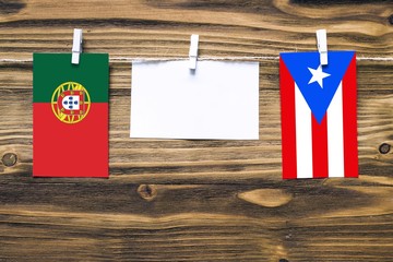 Hanging flags of Portugal and Puerto Rico attached to rope with clothes pins with copy space on white note paper on wooden background.Diplomatic relations between countries.