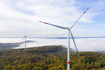 two wind turbines in colorful autumn forest with fog in the background