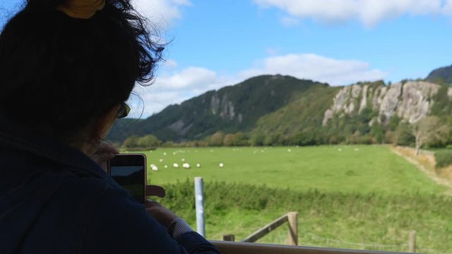 Woman, train passenger standing by the window and taking landscape pictures with her smartphone.