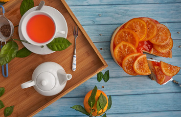 Top view and close-up of a cold homemade orange pie with candied orange on the surface and orange jam accompanied by a piece of orange pie, one fresh orange with green leaves, a tray with a teapot, a 
