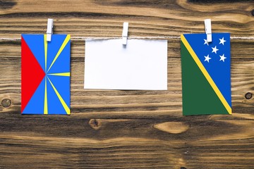 Hanging flags of Reunion and Solomon Islands attached to rope with clothes pins with copy space on...