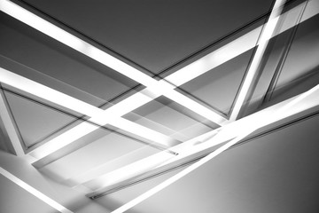 Lines of daylight lamps glowing in darkness. Double exposue of modern architecture or interior. Abstract black and white geometric background with hi-tech luminous polygonal and triangular structure.