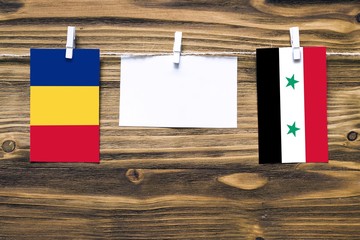 Hanging flags of Romania and Syria attached to rope with clothes pins with copy space on white note paper on wooden background.Diplomatic relations between countries.