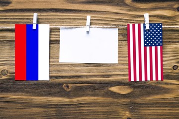 Hanging flags of Russia and United States attached to rope with clothes pins with copy space on white note paper on wooden background.Diplomatic relations between countries.
