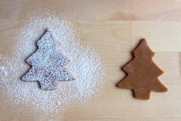 Two brown ginger dough cutted in christmas tree forms sprinkled with flour lies on the table