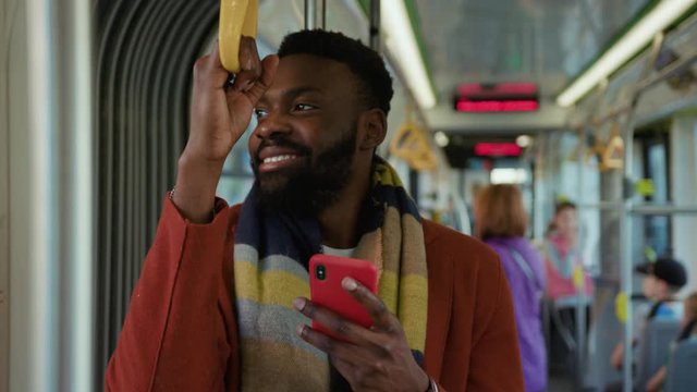 Smiling african american man use smartphone stand in tram look around happy traffic typing handsome passangers stylish transportation using way internet online texting guy slow motion