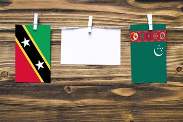 Hanging flags of Saint Kitts And Nevis and Turkmenistan attached to rope with clothes pins with copy space on white note paper on wooden background.Diplomatic relations between countries.