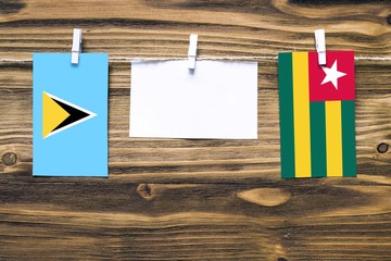 Hanging flags of Saint Lucia and Togo attached to rope with clothes pins with copy space on white note paper on wooden background.Diplomatic relations between countries.