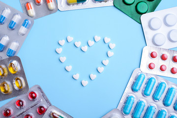 Heart frame made of pills on blue color background, flat lay with space for text
