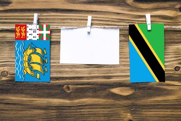 Hanging flags of Saint Pierre And Miquelon and Tanzania attached to rope with clothes pins with...
