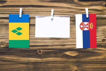 Hanging flags of Saint Vincent And The Grenadines and Serbia attached to rope with clothes pins with copy space on white note paper on wooden background.Diplomatic relations between countries.