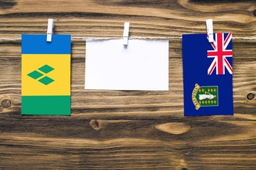 Hanging flags of Saint Vincent And The Grenadines and British Virgin Islands attached to rope with clothes pins with copy space on white note paper on wooden background.Diplomatic relations.