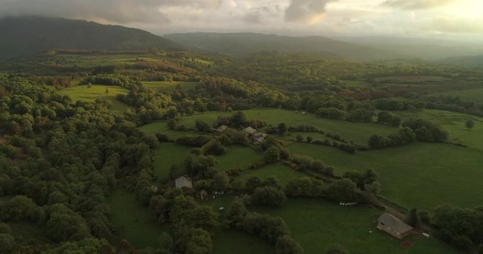 Aerial: Houses surrounded with trees and plants on idyllic lush green landscape against cloudy sky during sunset - Galicia, Spain