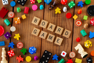 "Board Games" spelled out in wooden letter tiles. Surrounded by dice, cards, and other game pieces on a wooden background