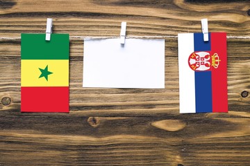 Hanging flags of Senegal and Serbia attached to rope with clothes pins with copy space on white note paper on wooden background.Diplomatic relations between countries.