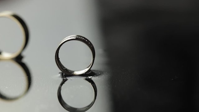 Wedding rings on black, white water surface. Groom ring rolling to bride's ring