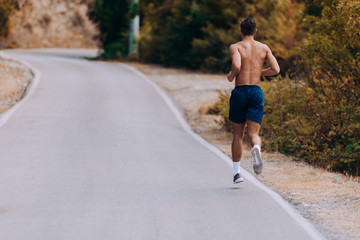 Full shirtless body portrait of a fit man running outdoors through mountain