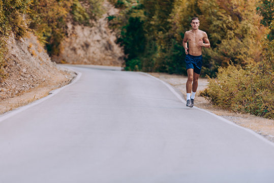 Male shirtless joger running in mountains under sunlight