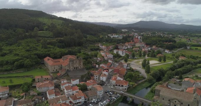 Aerial: Drone ascending over bridge over Sar River by buildings in town with mountains against cloudy sky - Padron, Spain