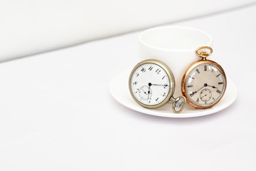 Pocket watches on a white mug. One gold and one silver watch.