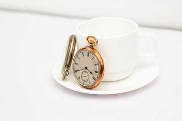 Pocket watches on a white mug. One gold and one silver watch.