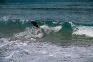 Young man riding a wave on a skimboard (a mix of surf and skate) in Cala Mesquida (Mallorca, Spain)