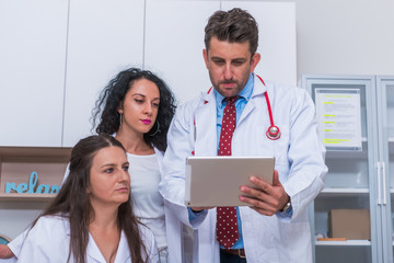 Two nurses ( female physicians ) and a male doctor looking in a tablet at the doctor's office while...