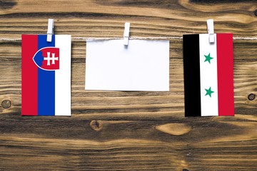 Hanging flags of Slovakia and Syria attached to rope with clothes pins with copy space on white...