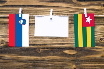 Hanging flags of Slovenia and Togo attached to rope with clothes pins with copy space on white note paper on wooden background.Diplomatic relations between countries.