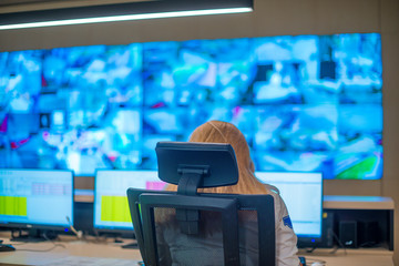 Female security guard sitting back and monitoring modern CCTV cameras in a  surveillance room.