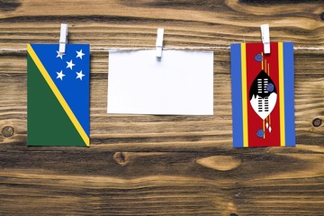 Hanging flags of Solomon Islands and Swaziland attached to rope with clothes pins with copy space on white note paper on wooden background.Diplomatic relations between countries.