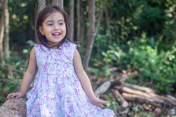 Pretty three year old girl, sitting on a stone of the field, laughs and looks happily off camera in...