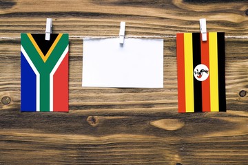 Hanging flags of South Africa and Uganda attached to rope with clothes pins with copy space on white note paper on wooden background.Diplomatic relations between countries.