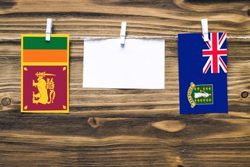 Hanging flags of Sri Lanka and British Virgin Islands attached to rope with clothes pins with copy space on white note paper on wooden background.Diplomatic relations between countries.