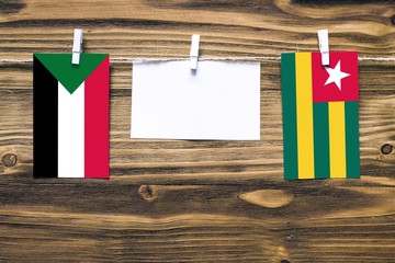 Hanging flags of Sudan and Togo attached to rope with clothes pins with copy space on white note paper on wooden background.Diplomatic relations between countries.