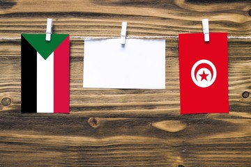 Hanging flags of Sudan and Tunisia attached to rope with clothes pins with copy space on white note paper on wooden background.Diplomatic relations between countries.