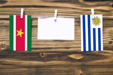 Hanging flags of Suriname and Uruguay attached to rope with clothes pins with copy space on white note paper on wooden background.Diplomatic relations between countries.