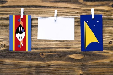 Hanging flags of Swaziland and Tokelau attached to rope with clothes pins with copy space on white note paper on wooden background.Diplomatic relations between countries.