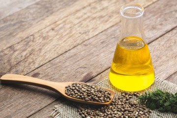  Hemp seeds in wooden spoon and hemp oil in a glass jar on brown wooden table. medical marijuana...
