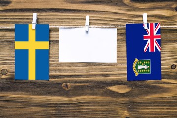 Hanging flags of Sweden and British Virgin Islands attached to rope with clothes pins with copy space on white note paper on wooden background.Diplomatic relations between countries.