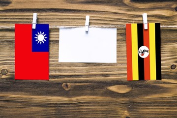 Hanging flags of Taiwan and Uganda attached to rope with clothes pins with copy space on white note paper on wooden background.Diplomatic relations between countries.