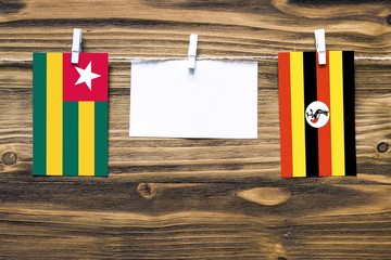 Hanging flags of Togo and Uganda attached to rope with clothes pins with copy space on white note paper on wooden background.Diplomatic relations between countries.